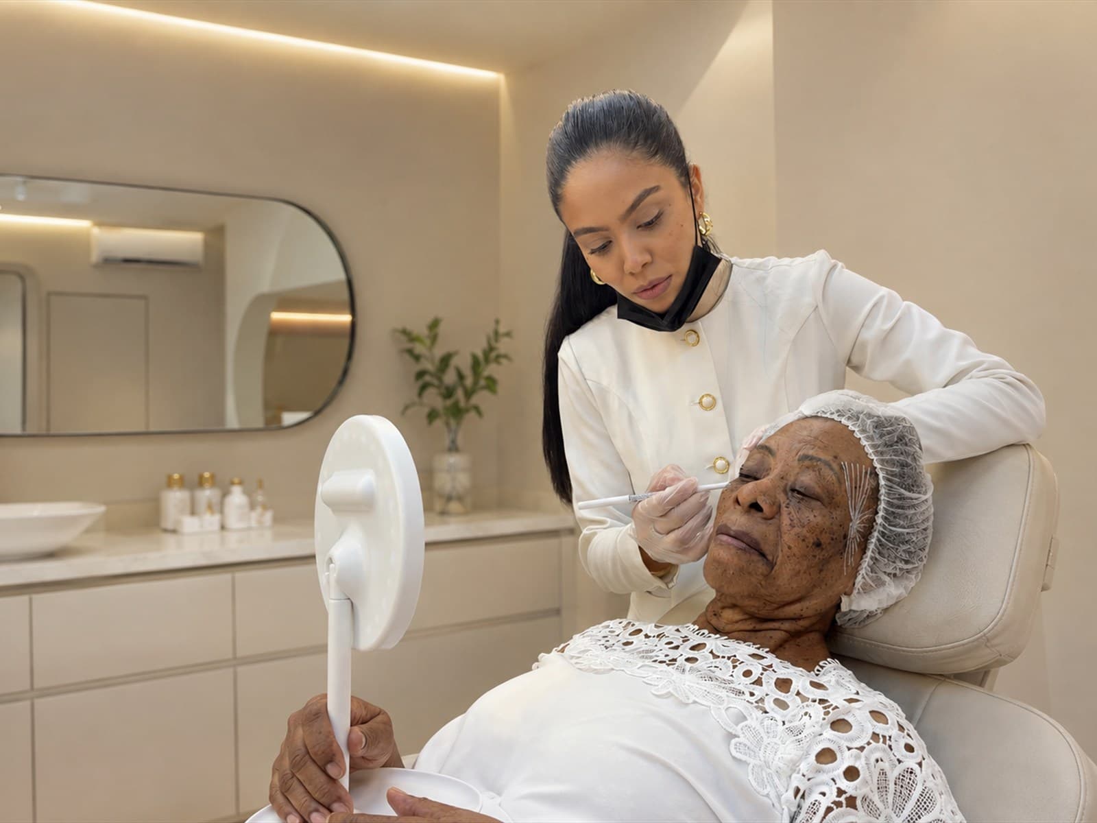 Profissional da VGLAM atendendo uma paciente com um espelho durante o tratamento com bioestimulador de colágeno.